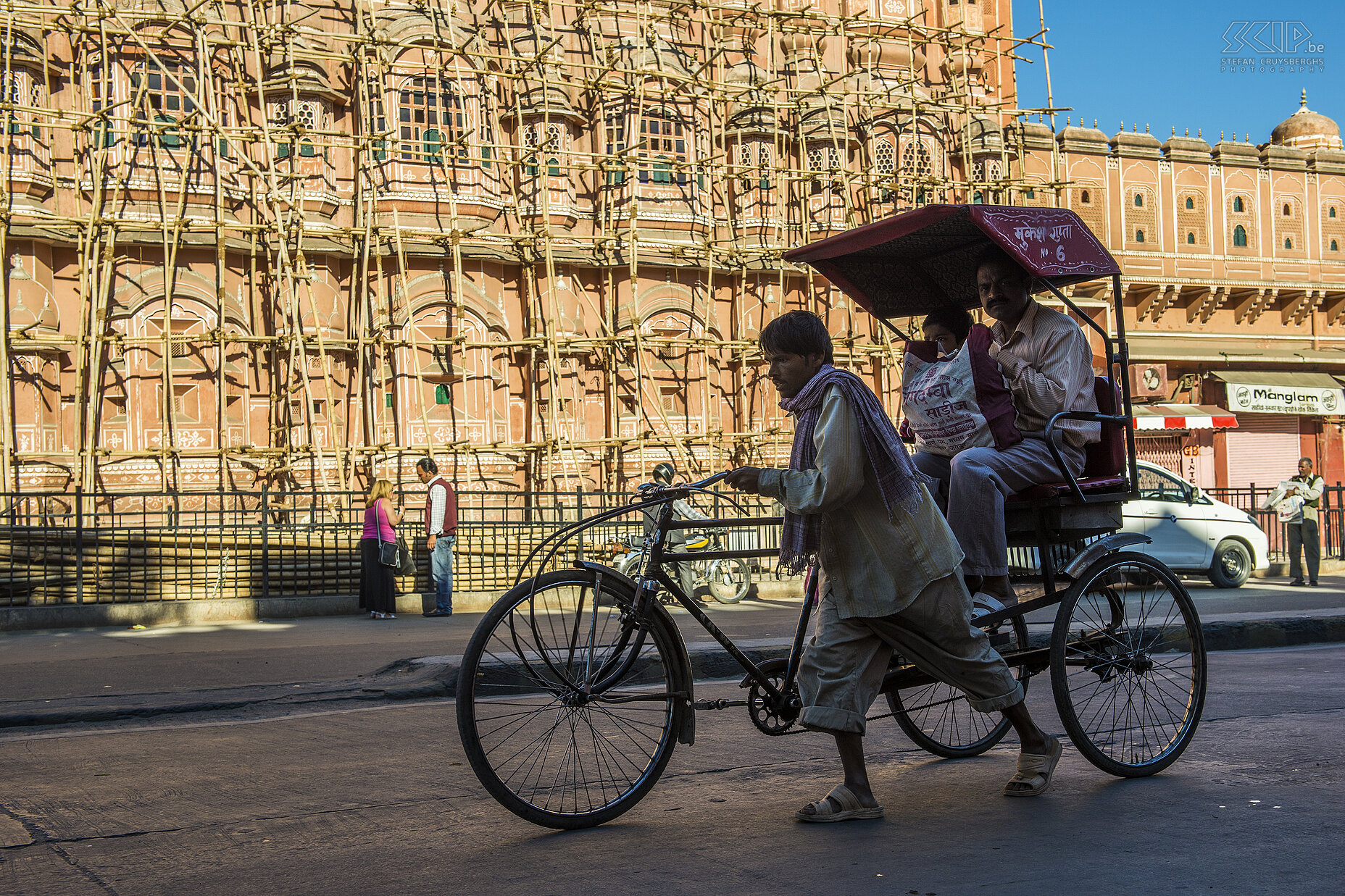 Jaipur - Riksja aan Hawa Mahal Het prachtige Hawa Mahal, oftewel het Paleis der Winden, telt 953 ramen, balkons en nissen verspreid over vijf verdiepingen. Het paleis werd in 1799 in opdracht van de toenmalige Maharaja Sawai Pratap Singh gebouwd en het gaf de vrouwen de kans om naar het straatbeeld en de processies te kijken zonden zelf gezien te worden. Bij ons bezoek stond het in de steigers. Stefan Cruysberghs